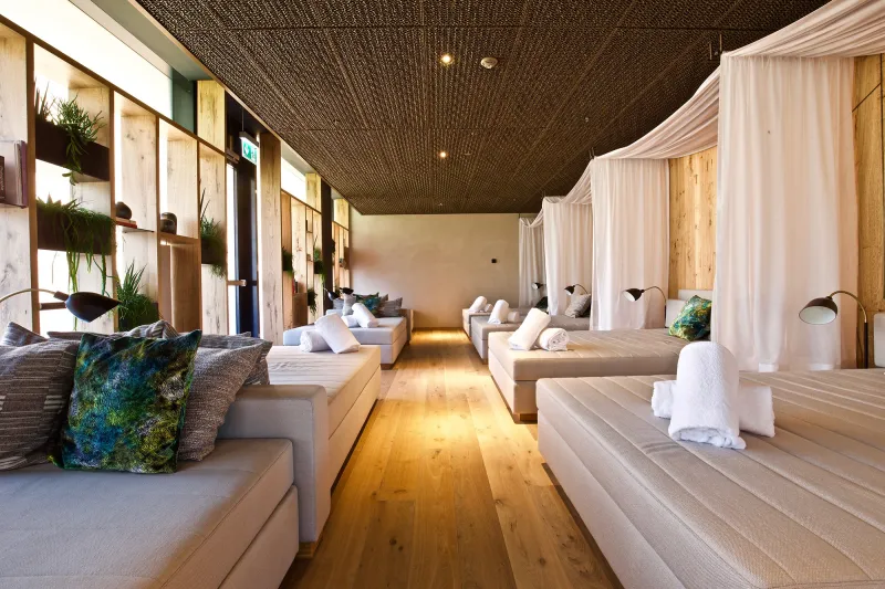 Streckmetall-Akustikdecke im The Stenna Spa in Flims The Stenna Spa in Flims. Ein heller Raum mit einer Streckmetall-Akustikdecke mit 3D-Elementen über einem Holzboden. Im Raum sind eine Art Sofas und Vorhänge zu sehen.